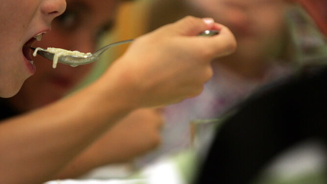 Un niño se lleva una cucharada de fideos a la boca en un comedor escolar.