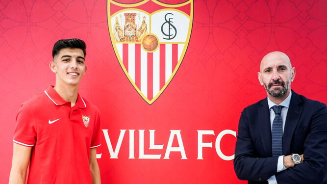 Alberto Flores, muy sonriente, posa con Monchi tras firmar su renovación ante el escudo del Sevilla.