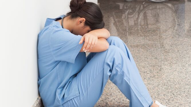 Una enfermera, cabizbaja, en el suelo de un centro sanitario.