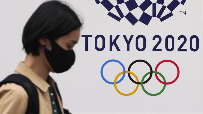 Una mujer con mascarilla pasa ante el logo de los JJOO de Tokio.