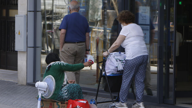 Una persona pide limosna a dos viandantes en una calle de Sevilla.