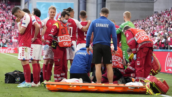 Los futbolistas de Dinamarca rodean a Eriksen en el césped.