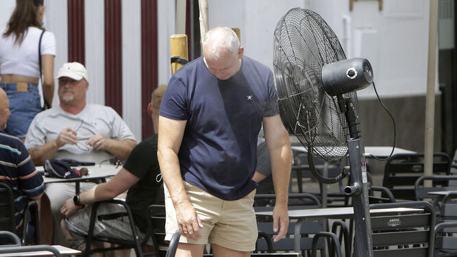 Un hombre se refresca delante de un ventilador en la terraza de un bar en Sevilla.