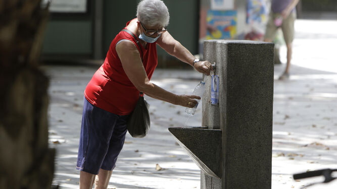 Una mujer se refresca en una fuente de Sevilla.