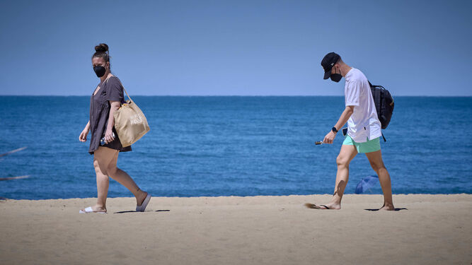 Dos personas caminan por la Playa de la Victoria de Cádiz con mascarillas.