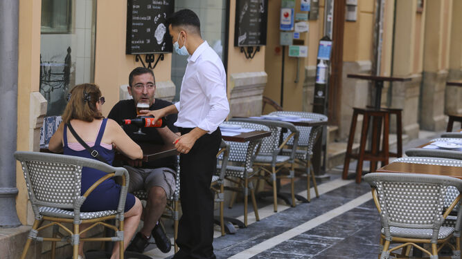 Un camarero atiende a una pareja de clientes en un negocio hostelero en el centro de Málaga