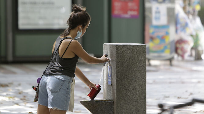 Una joven llena una botella en una fuente del centro.