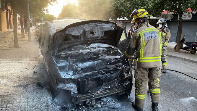 Los Bomberos apagan el incendio de uno de los coches quemados en la calle Venecia.