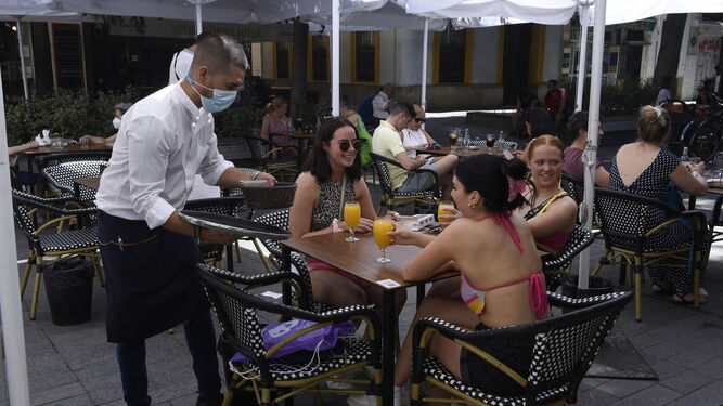 Varias jóvenes son atendidas en una terraza por un camarero con su mascarilla colocada.