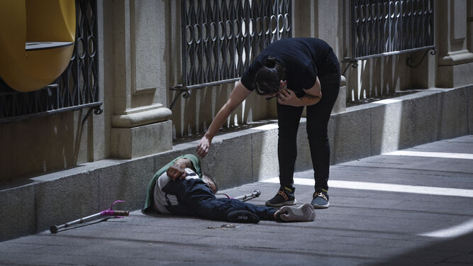 Una mujer atiende a una persona sin hogar tumbada en la acera en pleno centro.