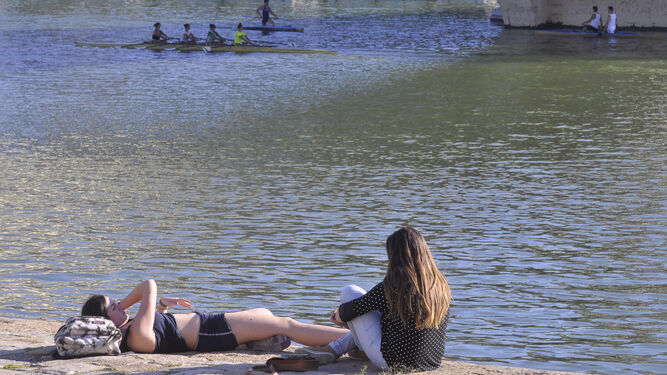 Dos jóvenes toman el sol en uno de los muelles del río en  Sevilla.