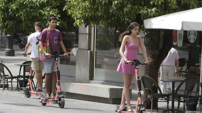 Dos usuarios en sendos patinetes de alquiler por el carril bici de la Avenida de la Constitución de Sevilla.