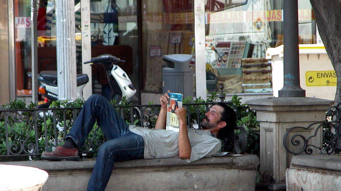 Un hombre lee tumbado en un banco