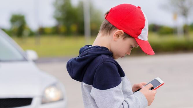 Un niño manipula un teléfono móvil en la calle.