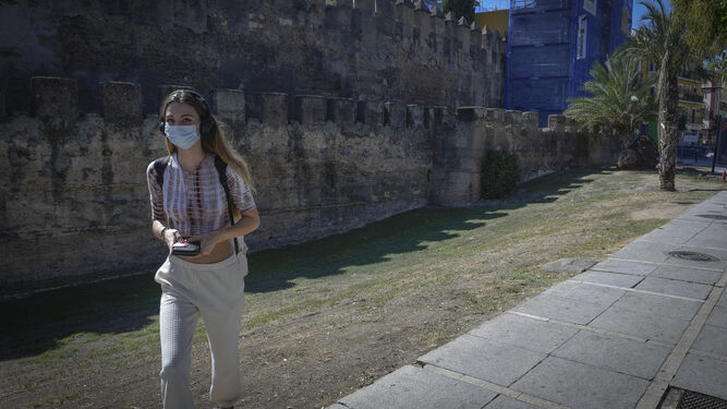 Una joven camina por el acerado junto a la Muralla de la Macarena.