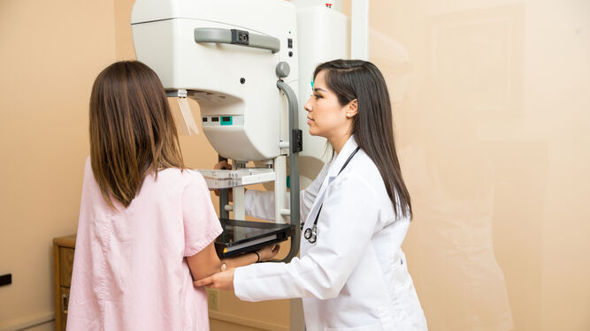 Una técnica de radiología ayudando a la paciente a colocarse frene a la máquina que realizará la mamografía.