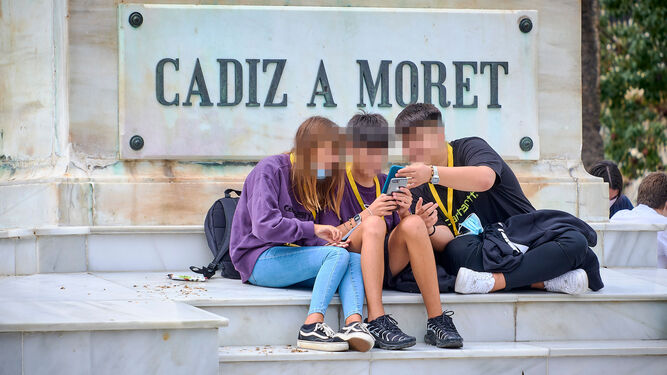 Tres jóvenes con sus móviles en una plaza de Cádiz.