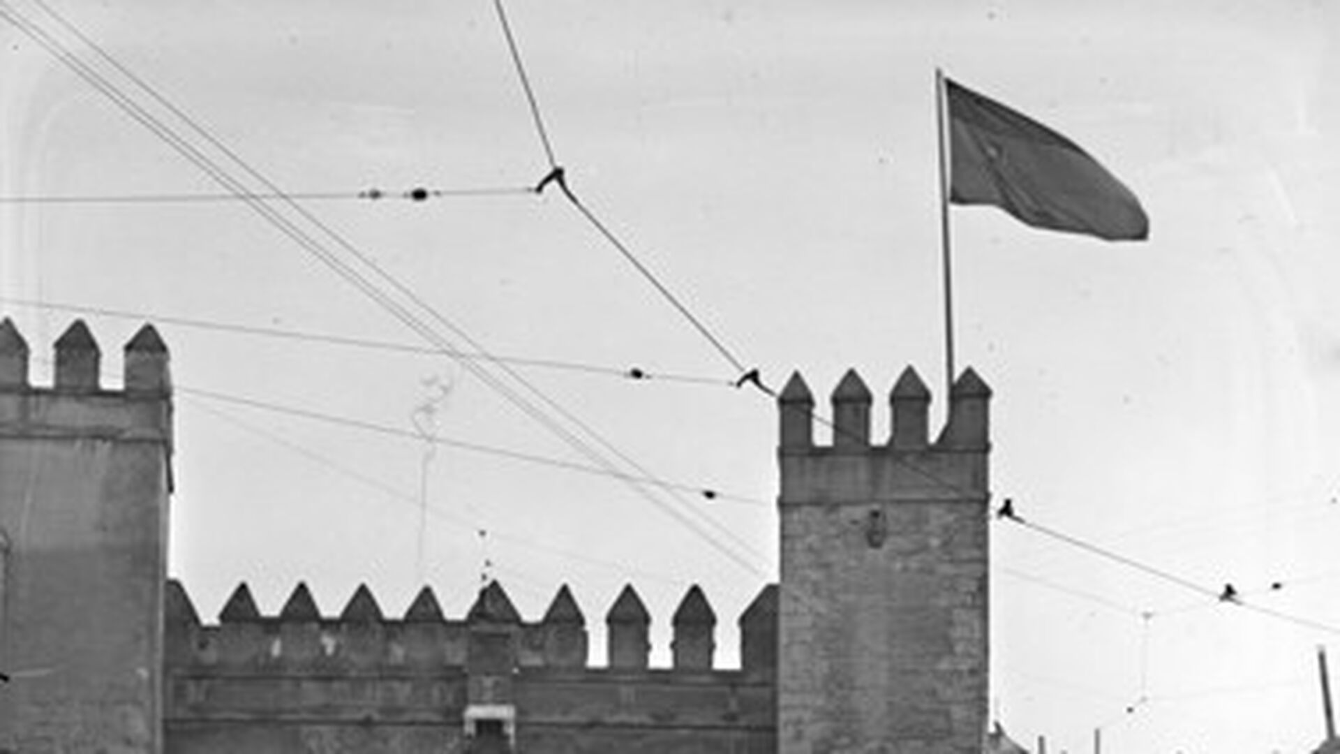 Puerta del Le&oacute;n del Alc&aacute;zar coronada por la bandera tricolor de la Segunda Rep&uacute;blica. Guardias de Asalto escoltan la entrada anta la expectaci&oacute;n del p&uacute;blico asistente a la entrega oficial del Alc&aacute;zar al Ayuntamiento de Sevilla el 31 de octubre de 1931.