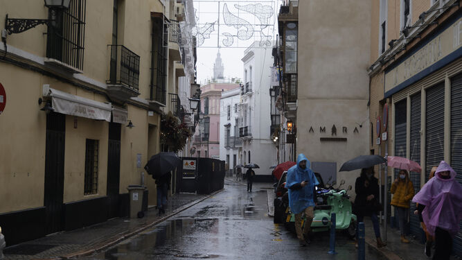 Varias personas corres para protegerse de la lluvia en el centro de Sevilla.