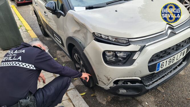Un policía local de Sevilla observa los daños en el vehículo.