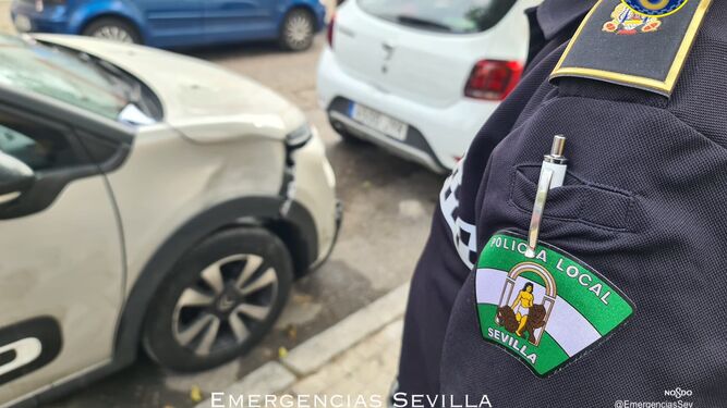 Un policía local de Sevilla, con el coche implicado en el accidente.