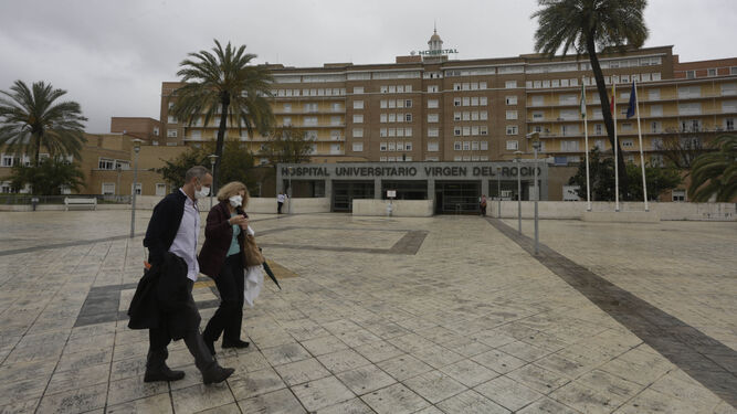 Dos personas caminan por el entorno de la entrada principal del Hospital virgen del Rocío.