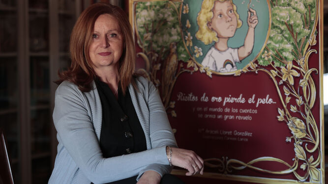 La profesora y escritora, Araceli Lloret, posa junto al cartel del libro 'Ricitos de oro pierde el pelo'.