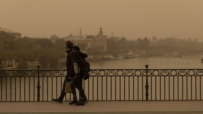 Dos personas caminan sobre la nube de polvo africano que envuelve estos días la ciudad.