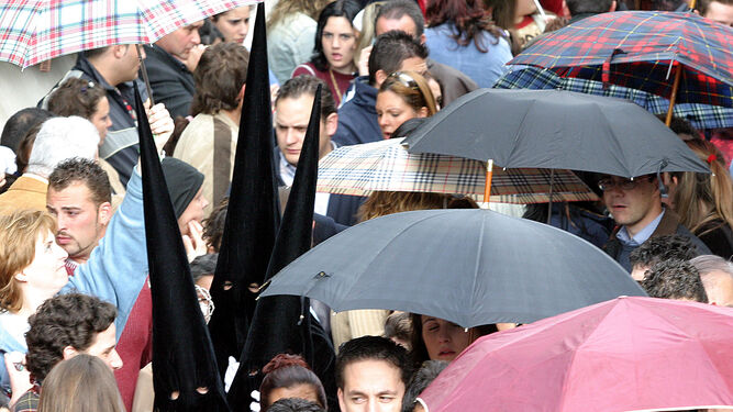 Nazarenos y público con paraguas refugiándose de la lluvia  de un Jueves  Santo