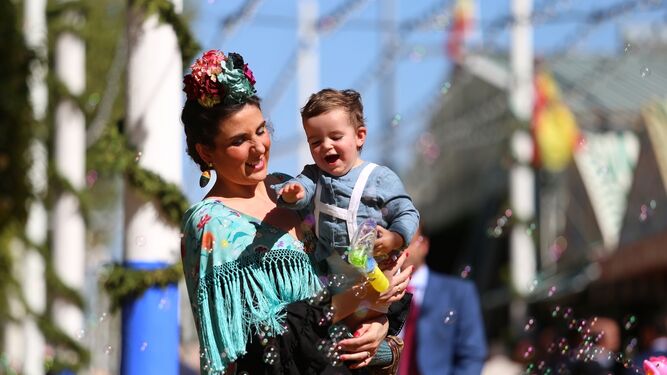 Una mujer vestida de flamenca y un niño que hace pompas de jabón. Imagen típica de la Feria de Sevilla.