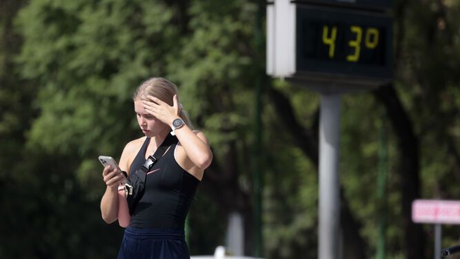 Una joven mira el móvil bajo un termómetro  que marca 43 grados.