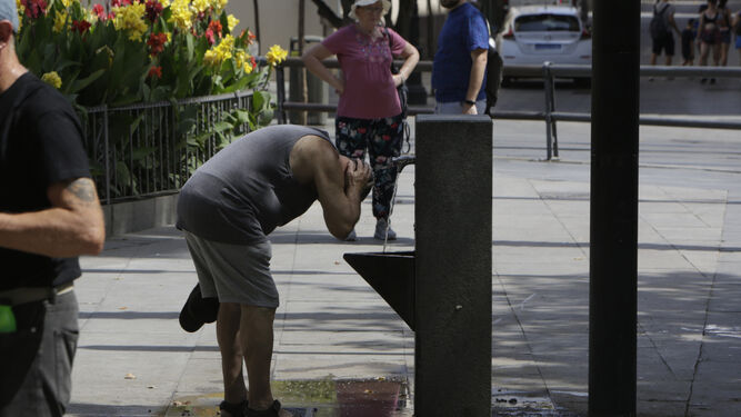Un hombre se refresca en una fuente pública durante los días en alerta roja por calor en Sevilla.