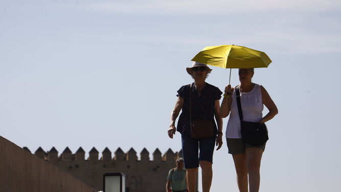 Unos turistas se protegen del sol con un paraguas mientras pasean por los alrededores del Puente Romano de Córdoba.