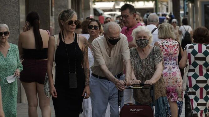 Una pareja de ancianos con mascarilla, en el centro de la imagen, entre numerosas personas sin ella por la calle.