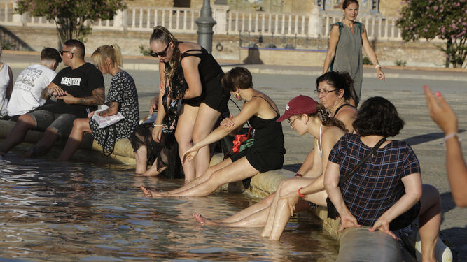 Un grupo de personas se refresca en la fuente de la Plaza de España.