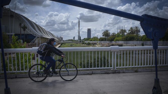Un ciclista cruza un puente de la Isla de la Cartuja con el cohete de la Expo al fondo.