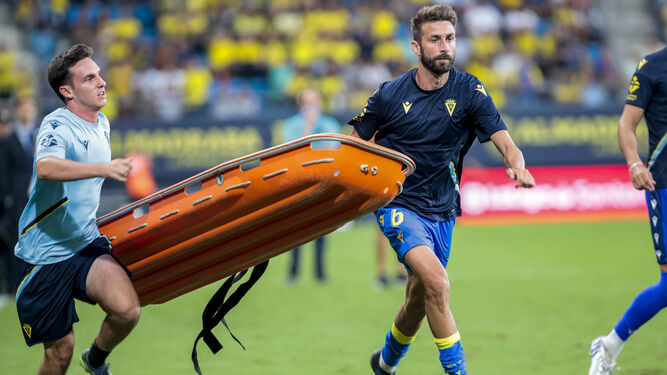 El futbolista del Cádiz José Mari, a la derecha, ayuda a transportar una camilla para la atención del aficionado.