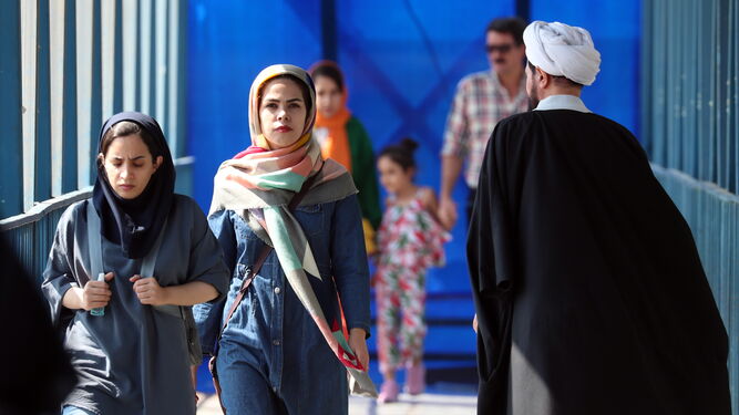 Mujeres iraníes pasan junto a un clérigo en una calle de Teherán.