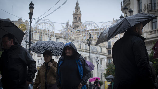 Viandantes ataviados con paraguas por el centro de Sevilla, con la Giralda de fondo .