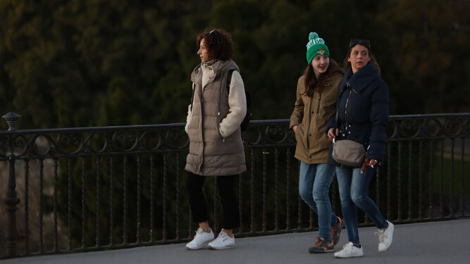 Tres mujeres pasean con ropa de abrigo por el puente de Triana.