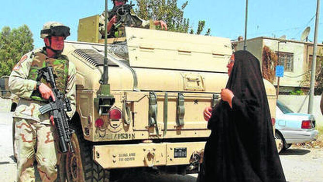 Fotografía de archivo de 2004, en la que una mujer iraquí que se cruza con soldados estadounidenses en Bagdad.