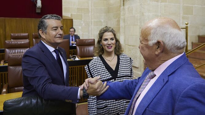 El presidente del Parlamento, Jesús Aguirre, saluda al consejero de Presidencia, Antonio Sanz, en presencia de  Ana Mestre