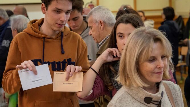 Un par de jóvenes con el voto preparado esperan la cola para depositarlo en la urna