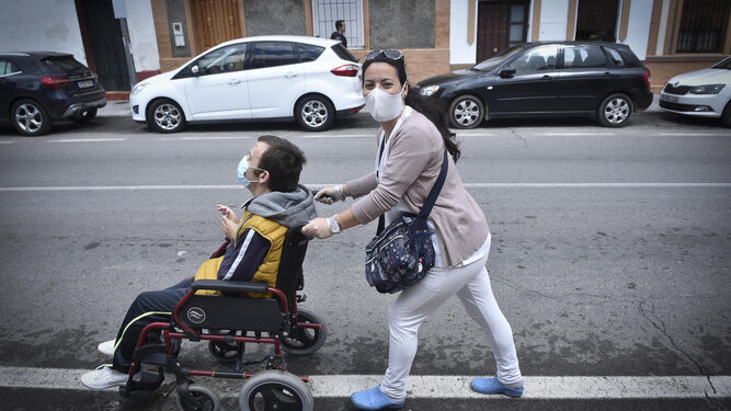 Una joven pasea a un chico discapacitado por una calle de Castilleja de la Cuesta.
