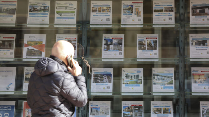 Un hombre pasa junto a la fachada de una inmobiliaria con oferta de pisos en venta.