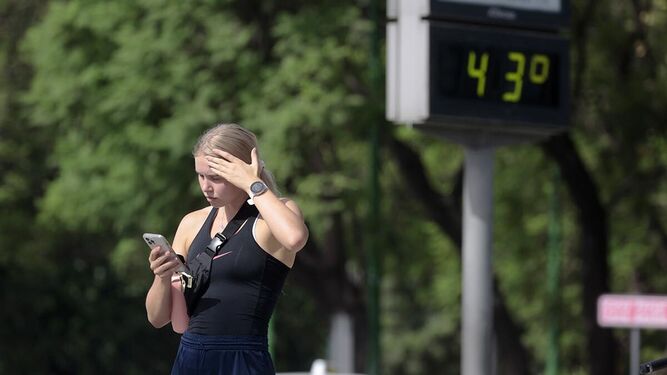 Una joven mira el móvil mientras intenta mitigar un poco el calor de Sevilla pasándose la mano por la frente.