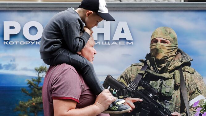 Un hombre con un niño sobre sus hombros pasa ante un cartel militar en San Petersburgo.