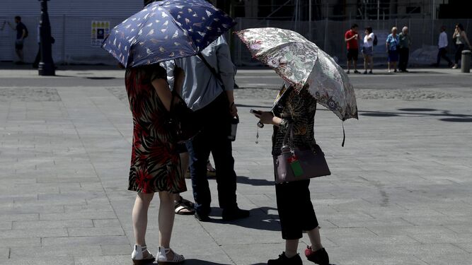 Varias personas se protegen del sol con paraguas en la Puerta del Sol de Madrid.