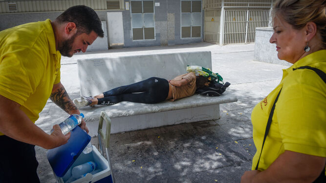 Dos trabajadores de la UMIES ofrecen agua a una mujer, que duerme en un banco en la calle.