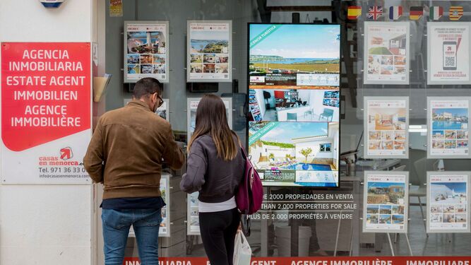 Una pareja observa anuncios de casas en venta en un escaparate